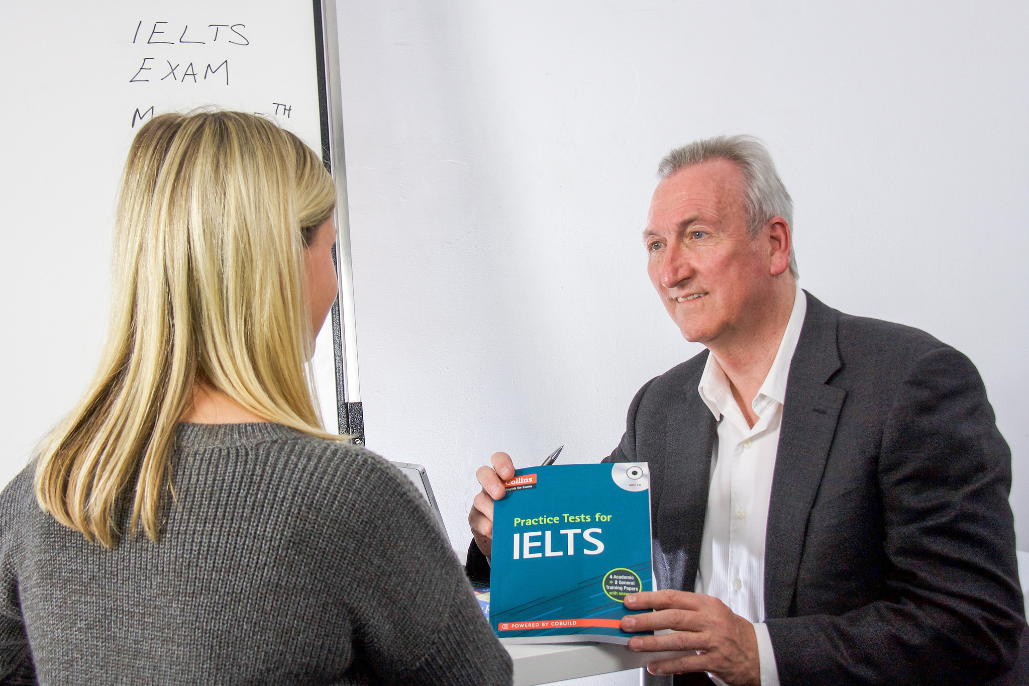 Mike sitting at a desk with a client holding a book of IELTS